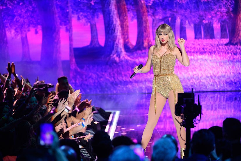 Taylor Swift wearing a golden-colored bodysuit on a stage in front of the crowd