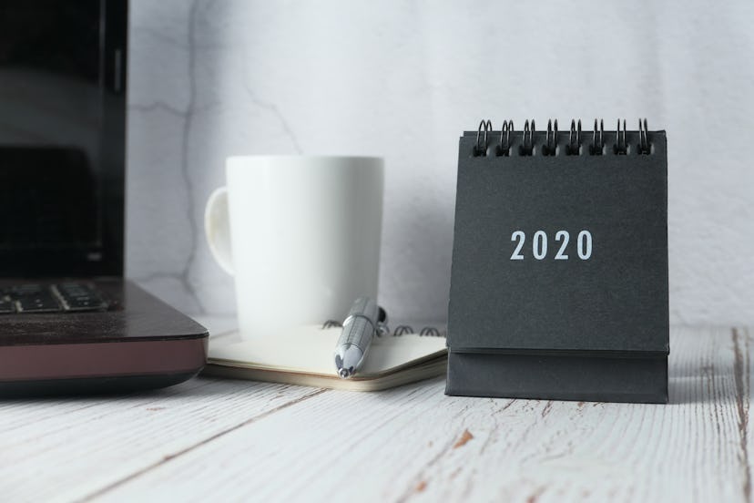 A black and white 2020 calendar sits next to a notebook and pen. Doodling about your success on a ca...