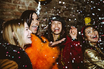 A group of stylish friends laughs and throws confetti in the air while out for New Year's Eve.