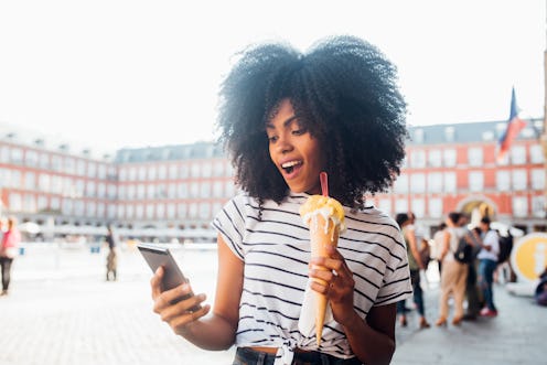 A woman traveling alone takes a selfie while eating an ice cream cone