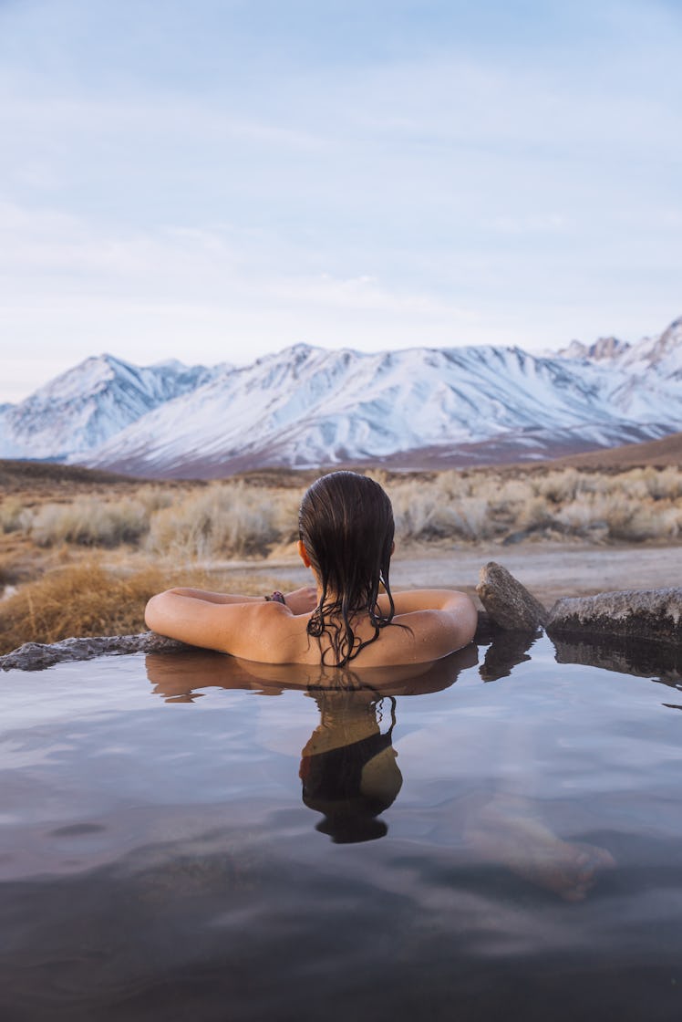 A woman soaks in a hot spring while looking at snowy mountains on an international trip.