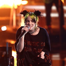 Bille Eilish wearing a black jumpsuit with red details and space buns hairstyle performing on stage 