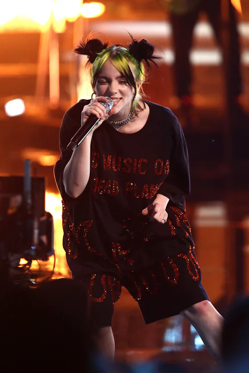 Bille Eilish wearing a black jumpsuit with red details and space buns hairstyle performing on stage