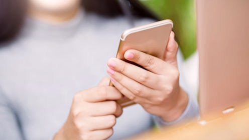 A person's body is blurred out by the camera while they hold their smartphone with both hands and lo...