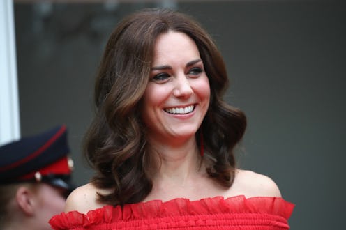 Kate Middleton in a red dress, smiling while posing for a photo