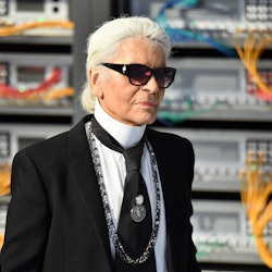 Karl Lagerfeld wearing his signature black suit with a tie, and black shades