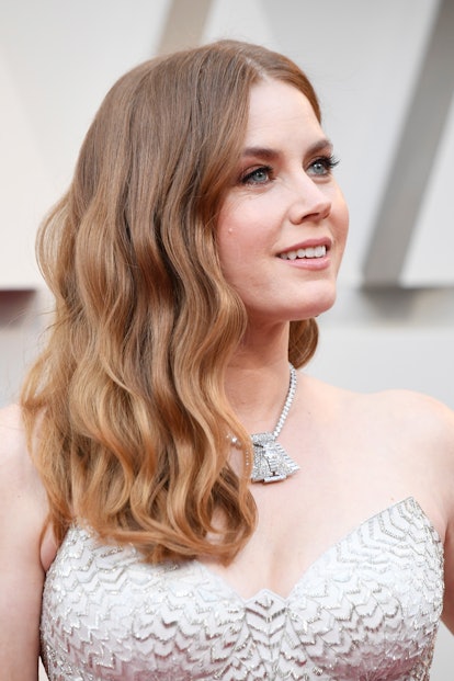 Amy Adams sporting natural-looking waves and subtle makeup and a sparkly metallic gown, with a chunk...
