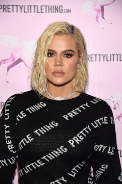 Khloé Kardashian posing in a black sweater with "pretty little thing" text signs