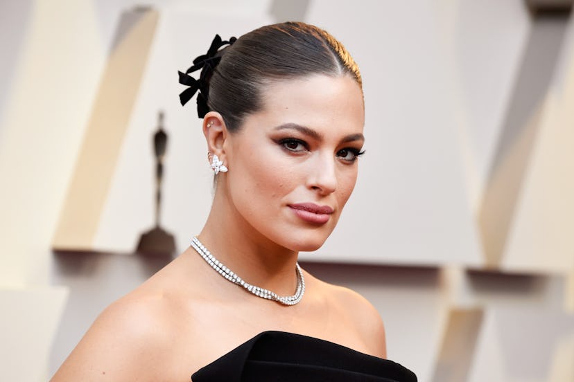 Ashley Graham in a strapless black gown, pearls, flower-shaped earrings and black bows in her up do