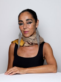Shirin Neshat posing in a black tanktop, a patterend scarf and large silver earrings