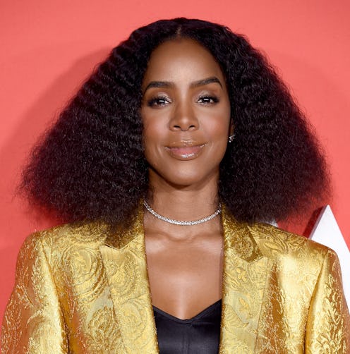 Kelly Rowland posing on the red carpet while wearing a gold blazer and a black top