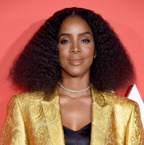 Kelly Rowland posing on the red carpet while wearing a gold blazer and a black top