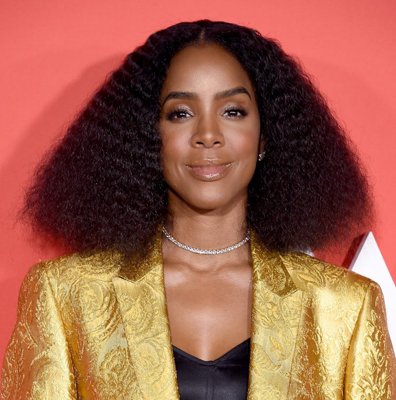 Kelly Rowland posing on the red carpet while wearing a gold blazer and a black top