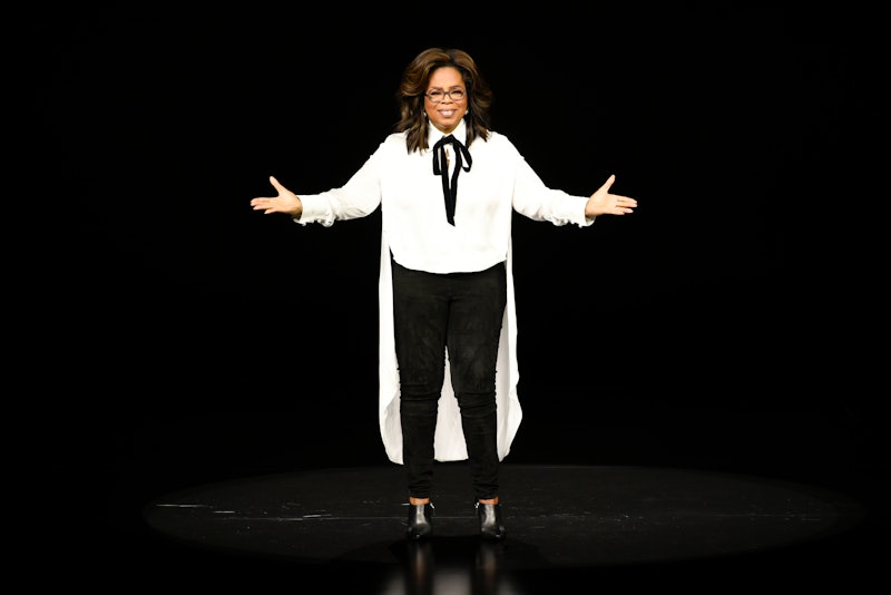 Oprah Winfrey during a speech in a white maxi shirt with bow, black pants and shoes