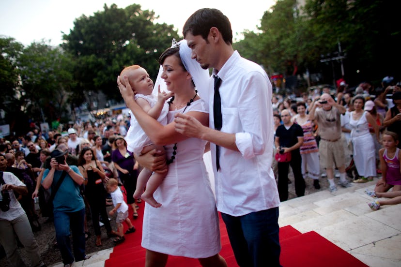 A bride and groom holding their baby in front of onlookers