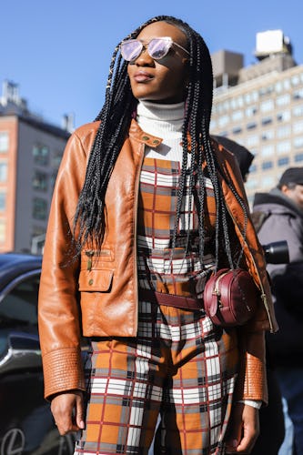 A woman posing in a tartan jumpsuit and in a brown leather jacket