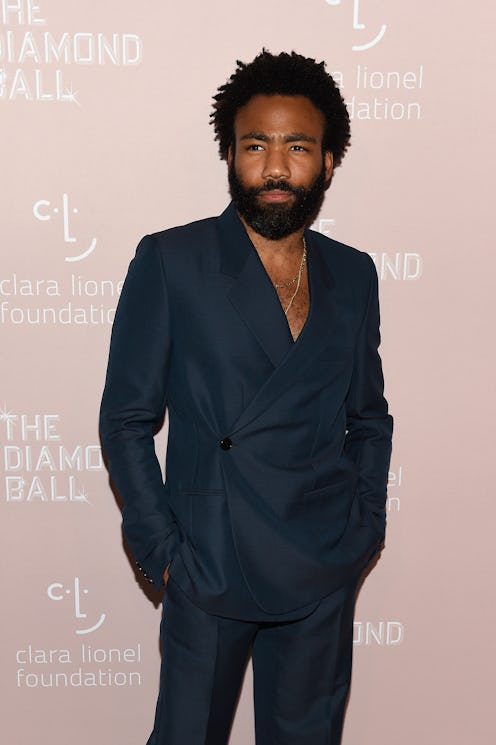 Donald Glover wearing a black suit with a silver chain