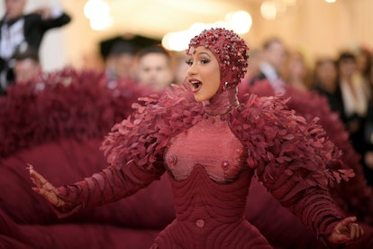 Cardi B at the Met Gala in an oxblood gem-encrusted gown with red leaves and a matching head piece f...