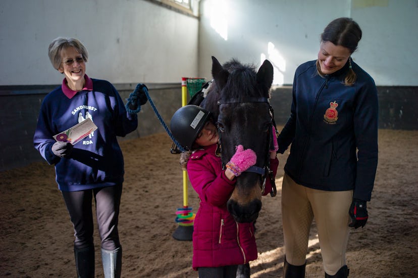 Three generations of woman horse riders standing next to and petting a horse