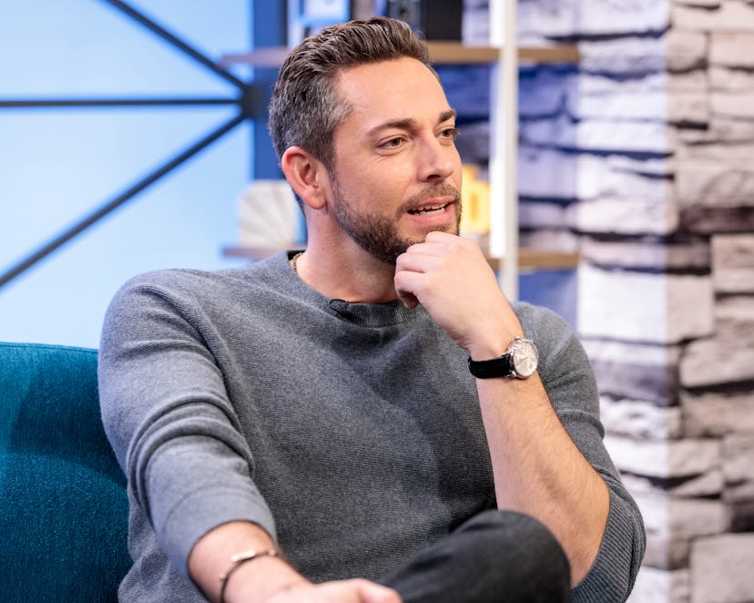 Zachary Levi as a guest at a talk show, wearing a grey sweater with his hand on his chin talking