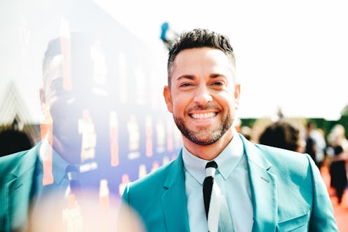 Zachary Levi at a red carpet for Shazam wearing a teal suit and smiling at the camera