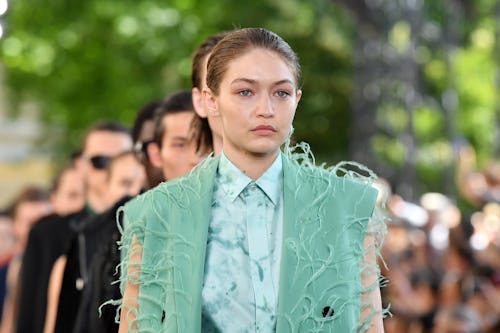 Gigi Hadid walking the runway in a green vest and blue button-up