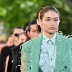 Gigi Hadid walking the runway in a green vest and blue button-up