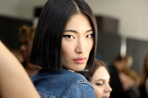 A model with a black bob, looking over her shoulder at the camera while wearing a jean jacket