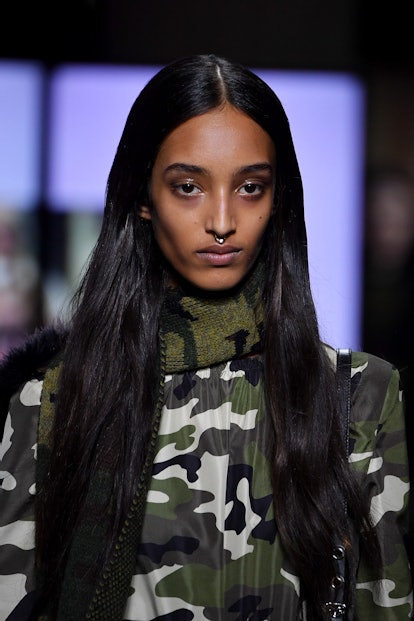 A model with long black hair wearing a camo print turtleneck sweater down the runway