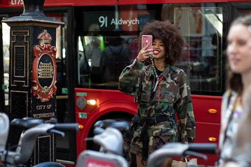 A woman in a camo print jacket takes a selfie in front of a red bus