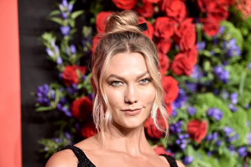 Karlie Kloss with her hair in a messy bun posing with a flower wall in her background
