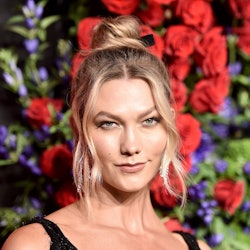 Karlie Kloss with her hair in a messy bun posing with a flower wall in her background