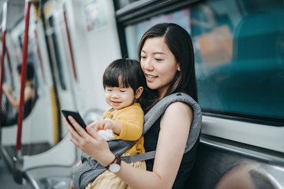 An Asian woman plays on her phone while holding her new nephew and riding the subway.