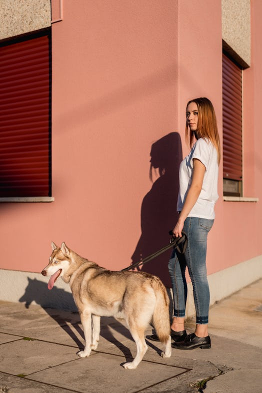 A woman poses against a pink wall in the city with her large dog.