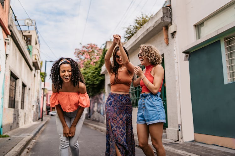 Three friends laugh and dance in the street of a colorful city while on vacation.
