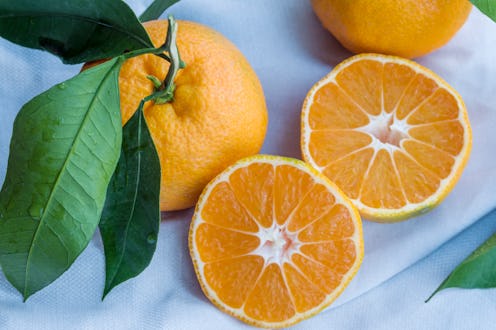 An orange, cut in half, sits next to a full orange, still with leaves on its stem. The best vitamins...