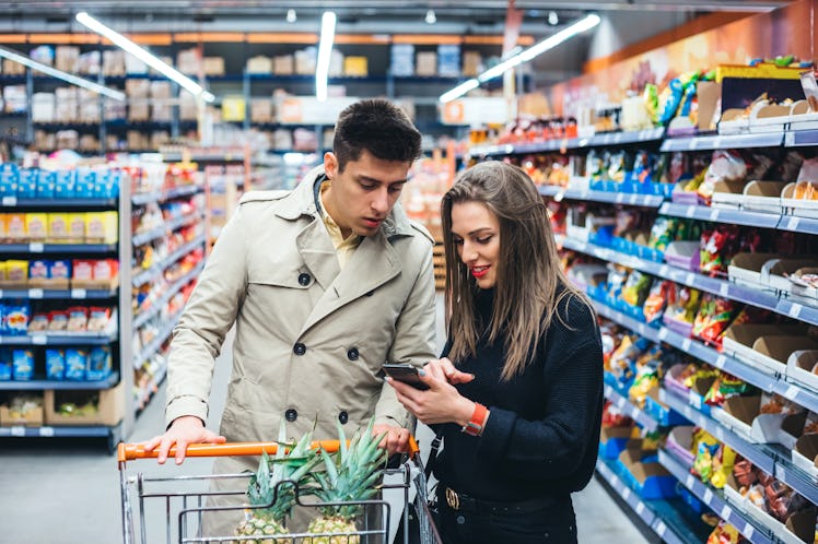 A young couple looks at a phone while going grocery shopping together.
