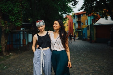 A young couple walks down the street of a colorful neighborhood while on vacation together. 