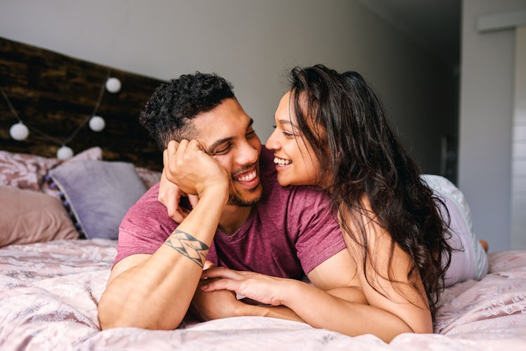 A young couple laughs while laying on their bed.