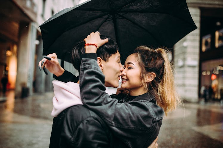 A young couple kisses under an umbrella on a rainy day in the city.