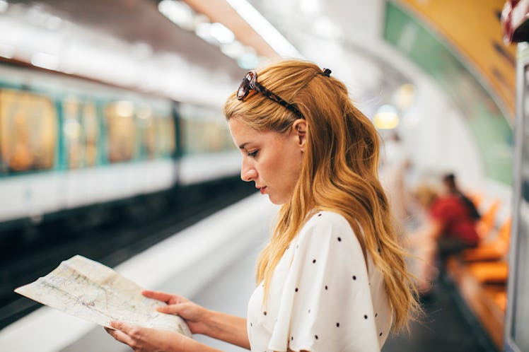 A red-haired woman looks at a map in a subway station while on vacation.