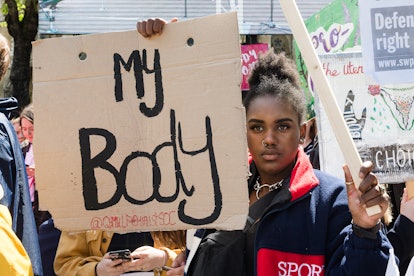 A young Black woman holds up a sign at a rally for reproductive rights that says "my body." The Trum...