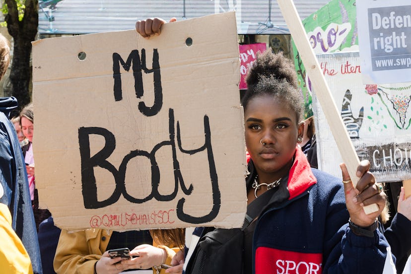 A young Black woman holds up a sign at a rally for reproductive rights that says "my body." The Trum...