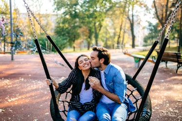 A happy couple sits on a large swing in the park.