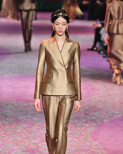 A female model walking in a golden couture pantsuit