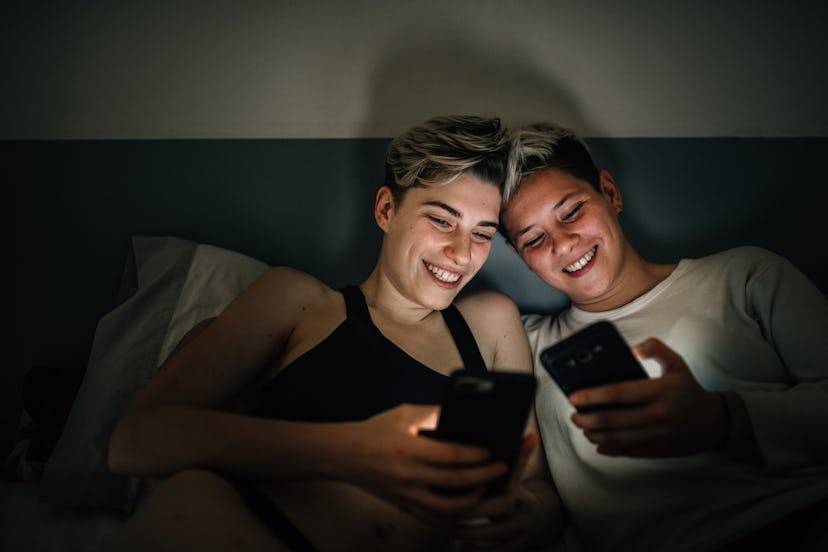 Two women look at phones in bed. Blue light from devices might interfere with melatonin production a...