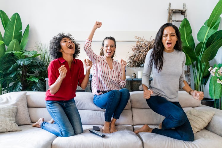 Three friends sit on a couch and cheer for their favorite team during the 2020 Super Bowl.