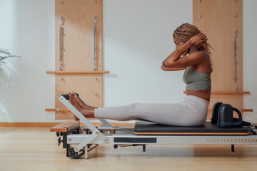 A person prepares to practice Pilates on a reformer. Pilates doesn't require equipment, but reformer...