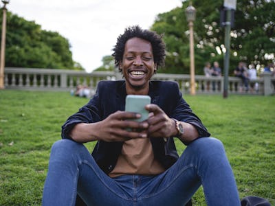 A man sitting, smiling, and looking at his phone while representing the life as a freelancer