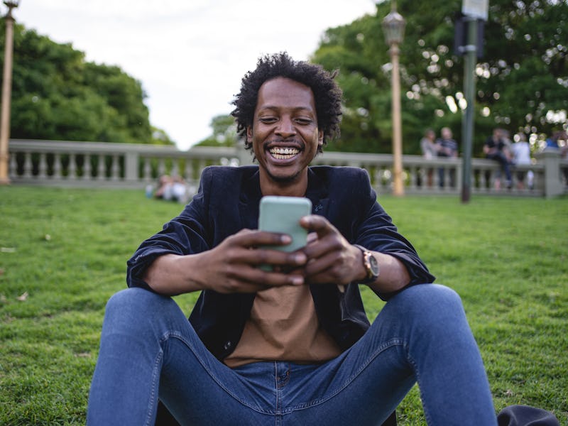 A man sitting, smiling, and looking at his phone while representing the life as a freelancer
